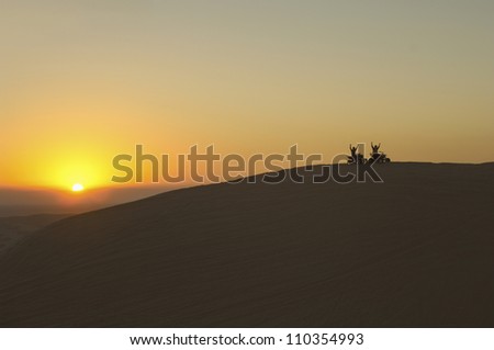 Two man riding quad bike in desert at sunset