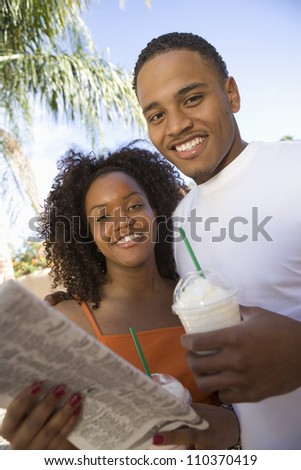 Portrait of a happy young couple with milk shakes holding newspaper