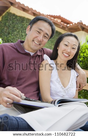 Happy asian couple reading novel outdoors