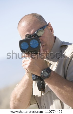 Portrait of a middle aged traffic officer looking through radar gun