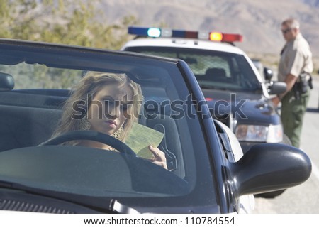 Young woman in car reading ticket with traffic cop in the background