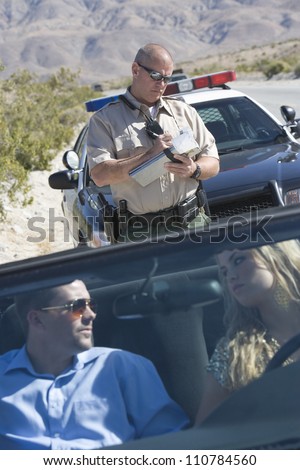 Couple in car looking at each other while traffic officer writing ticket in the background
