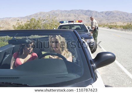 Young angry female friends reading ticket with traffic officer standing in the background