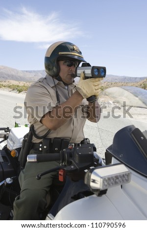 Police officer on motorbike monitoring speed though radar gun
