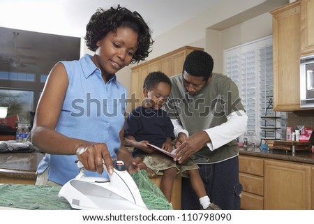 African American woman ironing clothes while man assisting son in homework