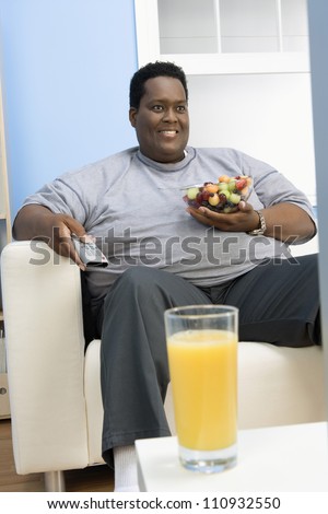 African American man eating fruits while watching television with a glass of juice in the front