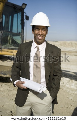 Portrait of a engineer wearing hard hat in front of a crane at construction site