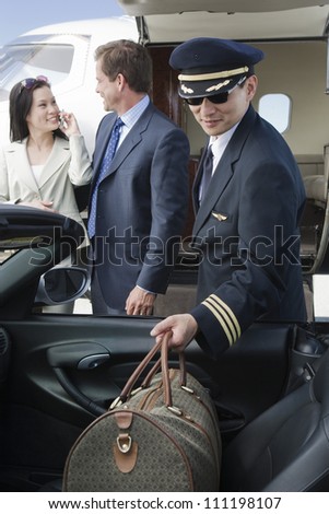 Airplane pilot putting luggage in car with business people in the background at airfield