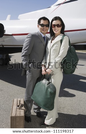 Full length of business couple standing together with luggage at airfield