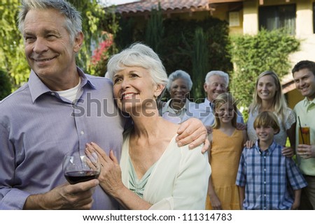 Portrait of senior couple standing with family and friend in background