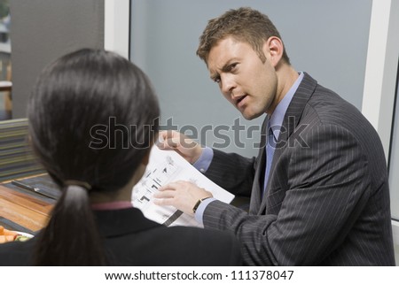 Businessman holding blue print and discussing with businesswoman in office