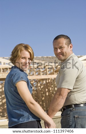 Portrait of happy middle aged couple in front of house under construction
