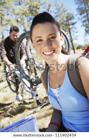 Portrait of a happy Caucasian woman with man repairing cycle in the background