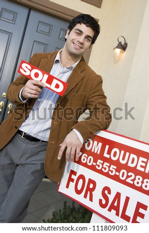 Man holding a sold sign board while standing in front of a new house