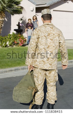 Rear view of soldier returning home with family waiting in background
