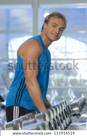 Man stands in front of dumbbells on rack at gym