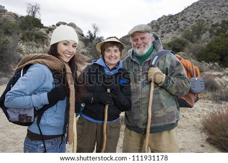Happy senior couple and daughter standing with sticks hiking
