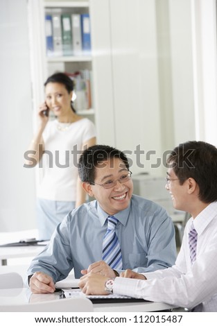 Two business colleagues in discussion with woman in the background