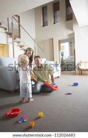 Happy parents watching daughter playing with toy at home