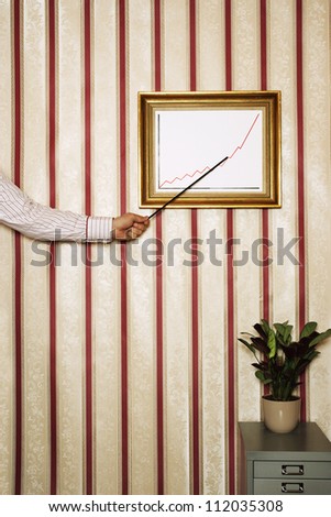 Man\'s hand pointing to framed graph on patterned wallpaper in office