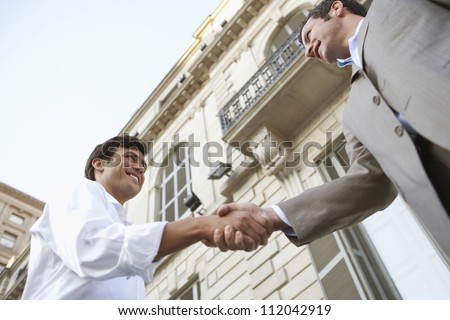 Two businessmen shaking hands for a successful deal with building in the background