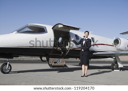 Female flight attendant standing in front of private jet on runway