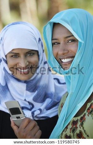Portrait of two Asian female friends in headscarf holding mobile phone