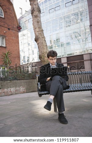 Young businessman working on laptop while sitting on bench