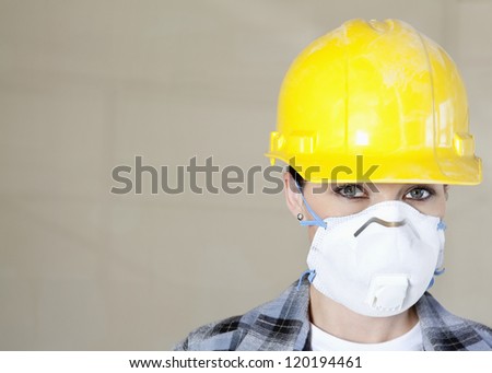 Portrait of female worker wearing dust mask and hardhat over colored background