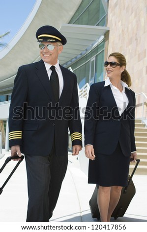 Happy airplane cabin crew walking together at the airport with bags
