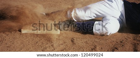 Motion blur low section show of a young baseball player sliding towards base on field