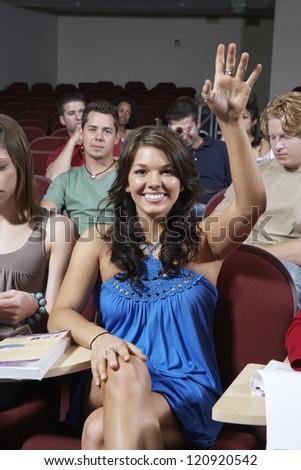 Portrait of a young female student raising hand in classroom