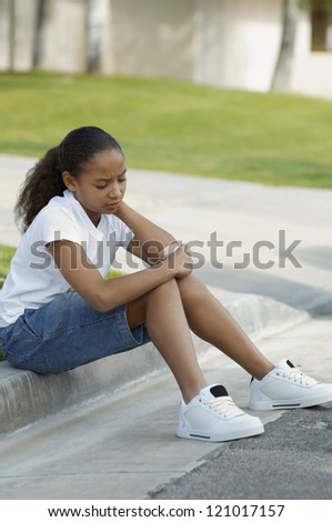 African American girl with band aid on arm sitting on curb