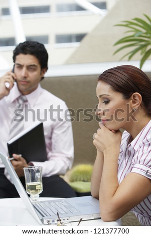 Business woman looking at laptop while colleague talking on cell phone in a restaurant