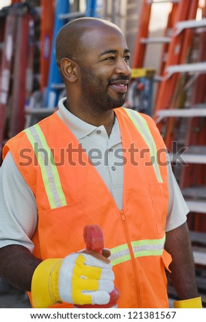 An African American construction worker wearing protective work wear with ladders in the background