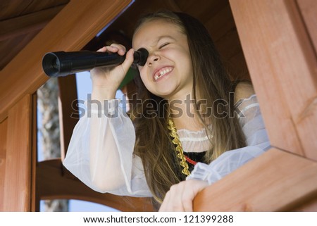 A happy young girl dressed as a pirate peering through telescope from window