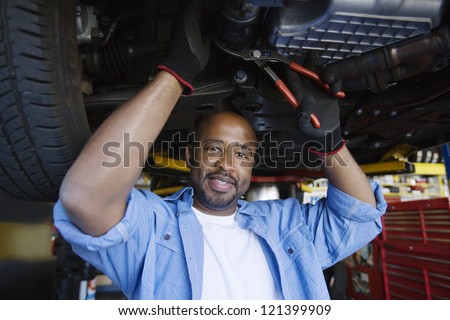 Portrait of a happy African American male mechanic repairing a lifted car In Garage