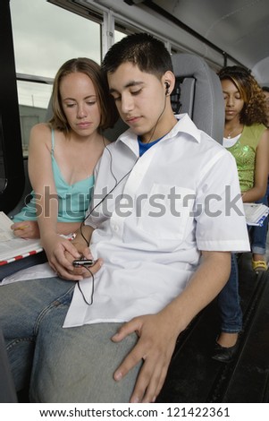 Young male student listening music while sitting besides female classmate in school bus