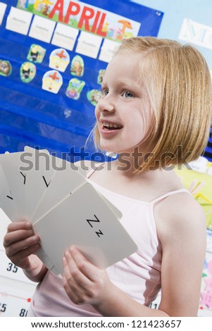 Cute little girl with alphabet cards in classroom