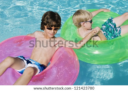 Male friends relaxing on inflatable ring while holding hands in pool
