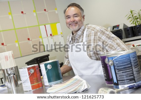 Portrait of a happy middle-aged sales clerk at counter with paint cans in hardware store