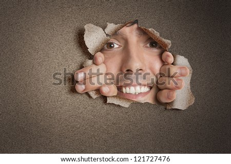 Portrait of a happy young Hispanic man peeking from ripped paper hole