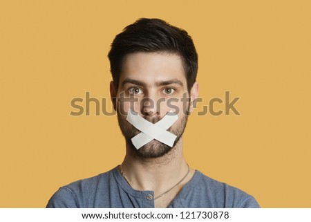 Portrait of a young man with tape on mouth over colored background