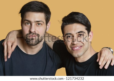 Portrait of two young male friends with arms around over colored background