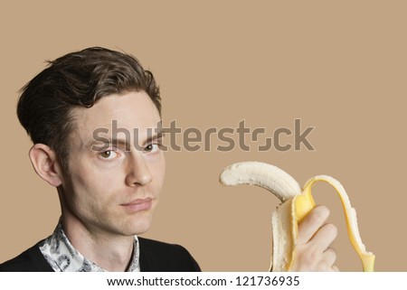 Portrait of a young man holding banana over colored background