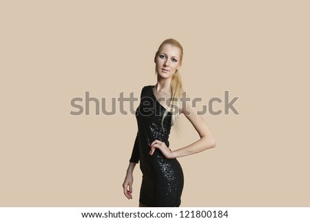 Portrait of a beautiful blonde woman wearing cocktail dress with hands on hips over colored background