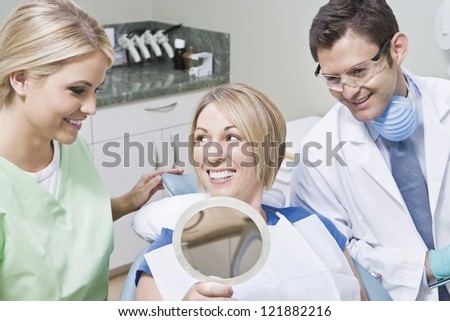 Happy dentistry team with female patient holding mirror in clinic