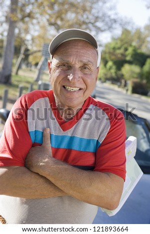 Portrait of a happy senior Caucasian man with arms crossed with car in the background