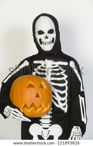 Hispanic boy in skeleton outfit holding a pumpkin isolated over white background