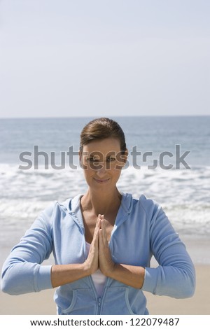 Portrait of woman in hooded top with hands clasped doing yoga exercise on beach